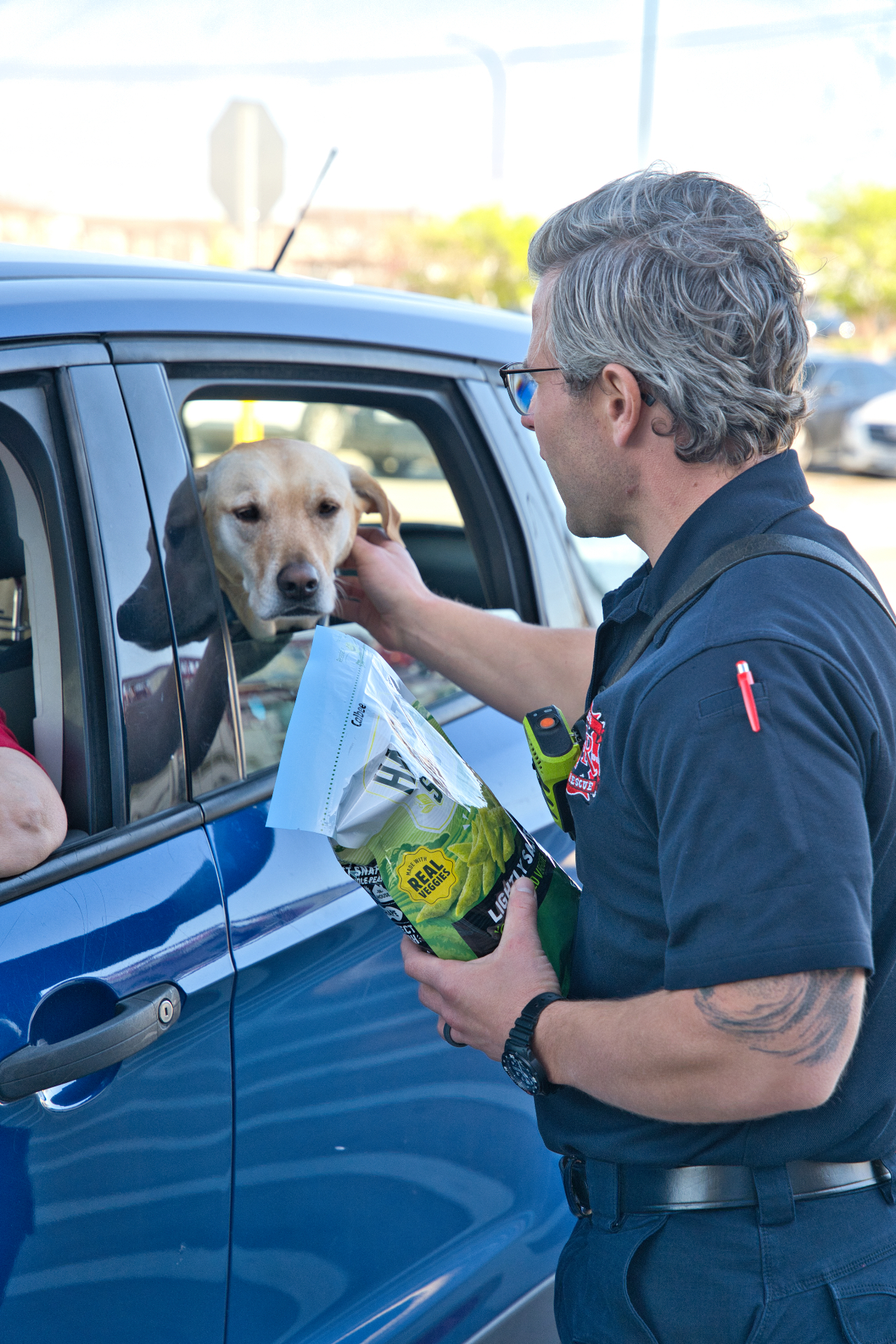 A Keller firefighter smiling as he pets a friendly Labrador leaning out of a car window
